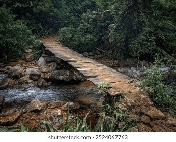 A small rustic wooden bridge crossing a clear mountain stream, surrounded by lush green forest and rocks - Powered by Shutterstock