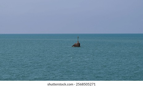 A small, rusty buoy with a beacon is floating in a calm sea under a clear blue sky.