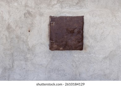 Small Rusty rectangular door on a weathered wall of coal storage. A closed, heavily rusted metal door with hinges is set in a rough, aged light gray wall. Rustic utility. Nobody.