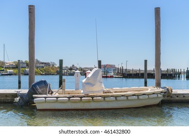 A Small Sailboat With Motor Sits Docked On The Pier Of A Quaint New England Fishing Village.