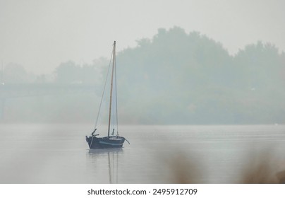 A small sailboat rests peacefully on a calm, misty lake, its sails billowing gently in the breeze, creating an ethereal and tranquil scene - Powered by Shutterstock