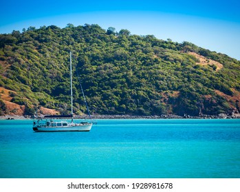 Small sailing boat on the turquoise ocean in front of a tree covered hill in Stanage, Queensland, Australia.
