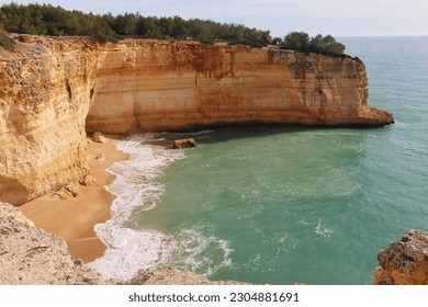 Small sandy beach surrounded by limestone cliffs at the Atlantic Ocean on a sunny winter day along the Seven Hanging Valleys Trail in southern Portugal.