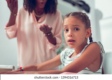Small scared girl. Face portrait of cute pretty small dark-haired girl feeling scared while her Afro-American mother with curly dark hair screaming at her