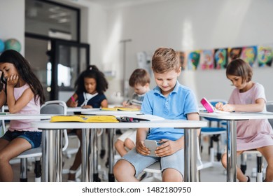 A small school boy with smartphone sitting at the desk in classroom, playing. - Powered by Shutterstock