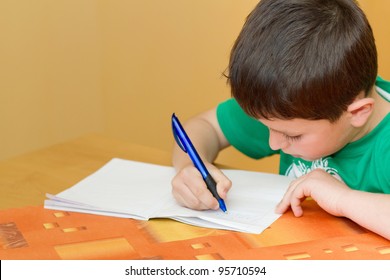small school boy writing homework from school in workbook