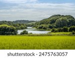 Small Scottish Loch or Lake in South Ayrshire with water surrounded by trees and viewed from across a field of grass in late summer