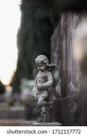 Small Sculpture Of A Baby Angel With Wings On A Stone Grave Tombstone. Old Dirty Worn Over Time