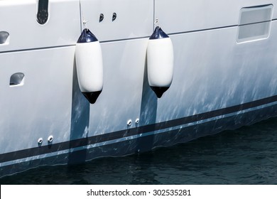 Small ship fenders hanging above luxury white pleasure yacht hull
