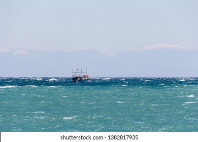 Small Ship Forging Ahead Through The Waves At Windy Day. Mediterranean Sea. Taurus Mountains Chain At The Hazy Background