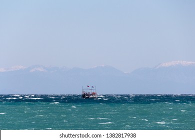 Small Ship Forging Ahead Through The Waves At Windy Day. Mediterranean Sea. Taurus Mountains Chain At The Hazy Background