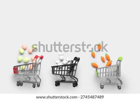 Small shopping carts with plasticine Easter bunnies, eggs and carrots on white background
