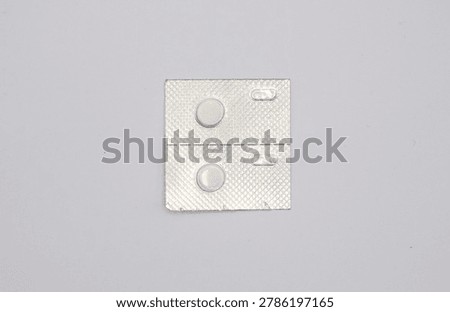 Small silver blister pack containing two white round contraceptive pills and two empty spaces, presented on a clean white surface, conveying concepts of medicine, birth control, or health management.