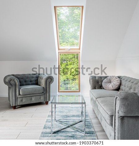 Small and simple attic lounge with window and gray, quilted sofa and armchair