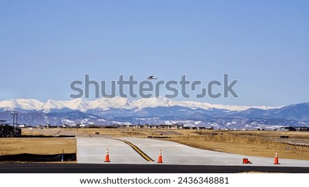 A Small Single Engine Airplane Taking Off From a Runway at the Far End of a Taxiway with Mountains in the Distance