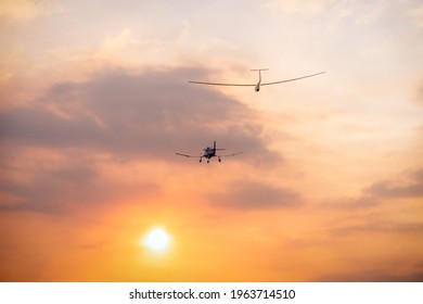 a small single engine plane pulling a glider into the setting sun