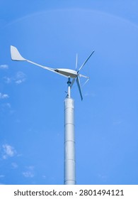 A small single wind turbine with multiple blades and a prominent tail vane mounted high on a pole against a deep blue sky.