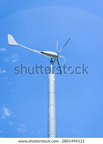 A small single wind turbine with multiple blades and a prominent tail vane mounted high on a pole against a deep blue sky.