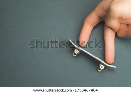 Small skateboard on color background. hand on tiny skate. fingers playing with fingerboard. home leisure concept. copy space