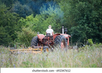 Small Smoke Billows From The Tractors Smoke Stack On A Little Country Farm. The Tractor Pulls A Brush Hog To Clear The Field.