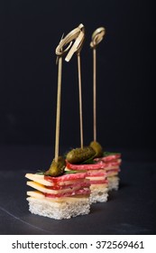 Small Snacks Canape With Salami, Cheese And Pickle On Skewer On A Black Slate Plate. Shallow Depth Of Field.