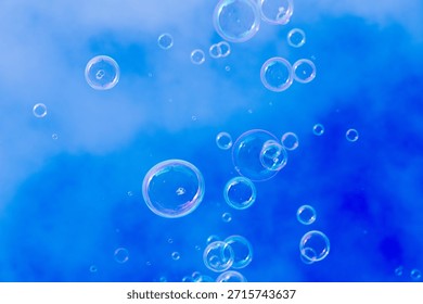 Small soap bubbles float upward against a bright blue sky with soft cloud patterns on a clear winter day.