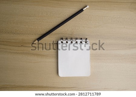 A small spiral notepad and a sharpened black pencil with an eraser lie on a wooden surface.