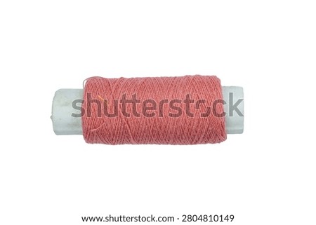 Small spool of pink sewing thread on white studio background. Essential tool for needlecraft and textile production. High quality cotton fiber for dressmaking kits.