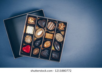 Small Square Box Of Chocolate Pralines And Truffles Assorted. Different Shapes And Fillings. Blue Toned Background, Directly Above.