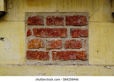 A small square of brick inside a yellow wall.
