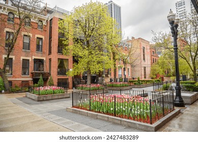 Small square with flower beds and a fountain surrounded by brick residentail buildings in old town Chicago on a cloudy spring day