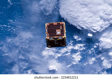 Small squared Satellite orbiting in outer space above planet earth deployed by the international space station. Digitally enhanced. Elements of this image furnished by NASA.