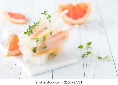A small stack of grapefruit thyme popsicles on a white wood slate table.
