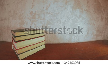 A small stack of multicolored books on a bright old brown table. Background old concrete wall.                               