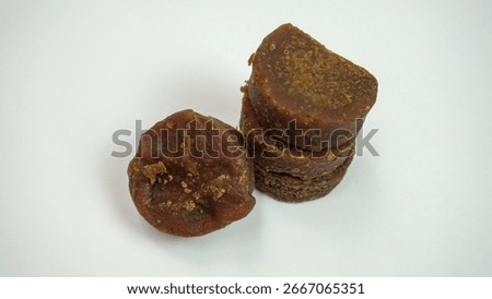 A small stack and a single piece of traditional Indonesian palm sugar (gula merah or gula jawa) on a white background. This sweetening ingredient is essential for various dishes and desserts.