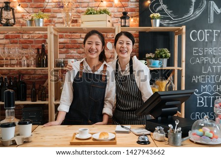 Small startup business owner concept. two successful young baristas women standing in bar counter in cafe. happy coffeehouse waitresses in aprons smiling confidently to camera in coffee shop.