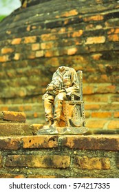 A Small Statue Of A Man Sitting On A Chair With His Head On His Knees Against A Brick Wall