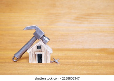 Small Steel Hammer And Nails By A Miniature Toy House Against A Wooden Background. Home Renovation Concept.