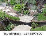 A small stepping stone syle bridge over a manmade stream in manicured tropical garden with rocks, grass and flowers, southeast Asia