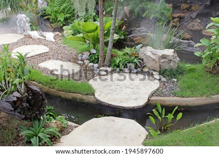 A small stepping stone syle bridge over a manmade stream in manicured tropical garden with rocks, grass and flowers, southeast Asia