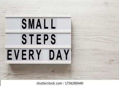 'Small steps every day' words on a lightbox on a white wooden background, top view. Overhead, from above, flat lay. Copy space. - Shutterstock ID 1736280440