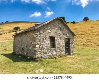 Small stone house on a plateau in the mountains with green meadows in the summer day in the sun with a door and a window - Shutterstock ID 2257844493