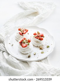 Small strawberry and pistachio pavlova meringue cakes with mascarpone cream, fresh mint over white backdrop, top view