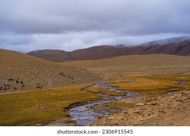 A small stream flows through the grassy fields at the foot of the mountain near Tso Kar, Thukje, Ladakh, India