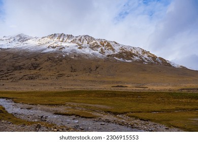 A small stream flows through the grassy fields at the foot of the mountain near Tso Kar, Thukje, Ladakh, India