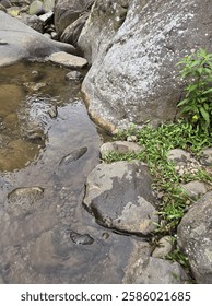 A small stream of water flows between large rocks. The water is murky and the rocks are jagged. The scene is peaceful and serene, with the sound of the water