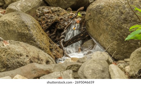 A small stream of water flows between two large rocks. The water is clear and the rocks are grey