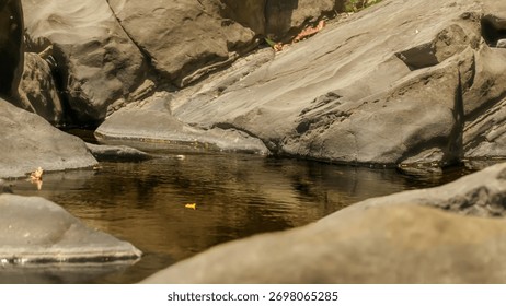 A small stream of water flows between two large rocks. The water is murky and brown, and the rocks are jagged and rough. The scene is peaceful and serene