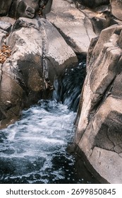A small stream of water flows down a rocky cliff. The water is clear and calm, and the rocks are jagged and rough. The scene is peaceful and serene