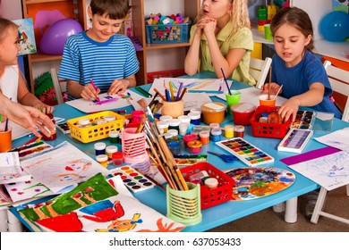 Small Students Girl And Boy Painting In Art School Class. Children Drawing By Paints On Table. Male Kid Shows His Drawing In Kindergarten. Many Children Draw Together.